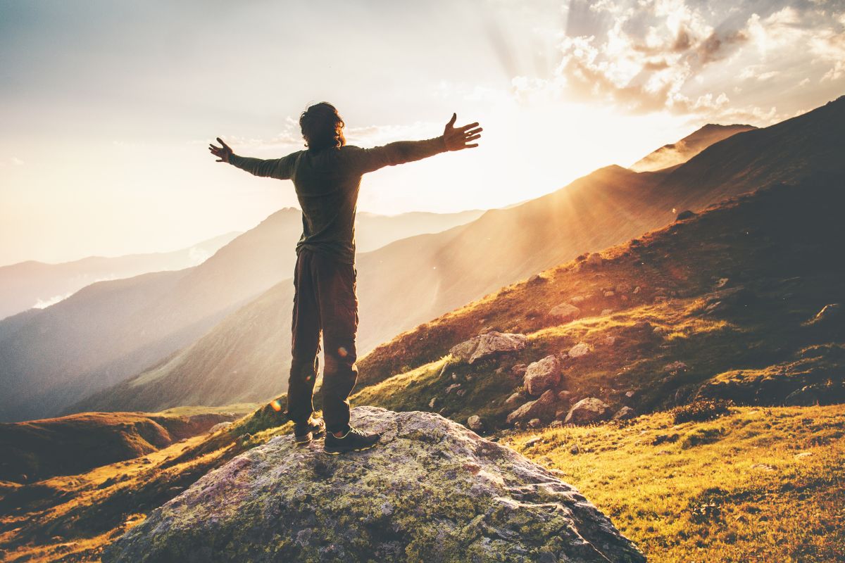 A man is standing on a hill shouting a positive affirmations for himself to start his day.