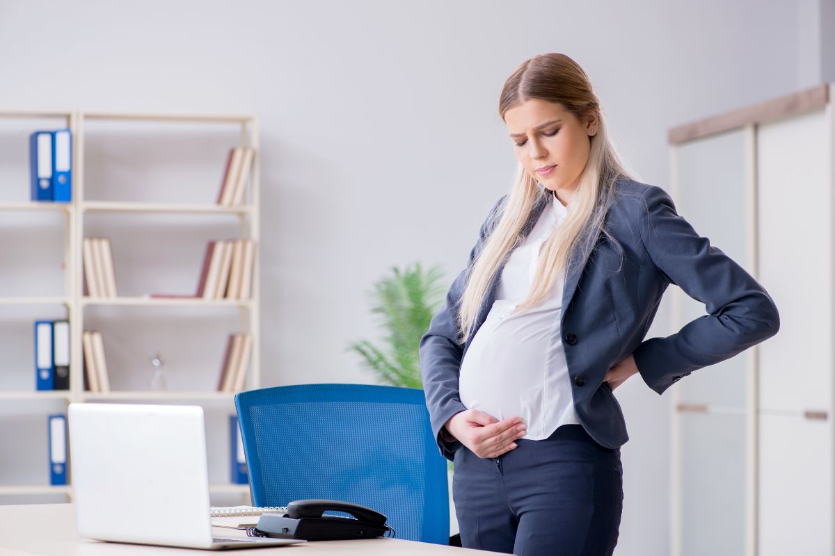 The pregnant woman is not comfortable with her office chair.